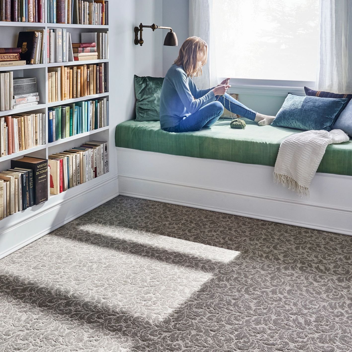 Woman knitting by the window of a room with gray patterned carpet from The Family Floor Store in Ellsworth, ME